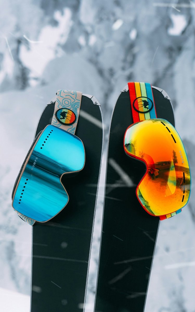 Ski goggles resting on a pair of skis in fresh snow